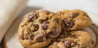 Μπισκότα με σταγόνες σοκολάτας σε ένα ταψί με λαδόκολλα, φρεσκοψημένα και χρυσαφένια, έτοιμα να κρυώσουν.