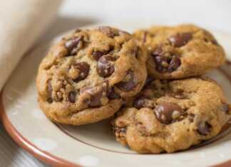 Φρεσκοψημένα μπισκότα με σταγόνες σοκολάτας σε σειρά πάνω σε λαδόκολλα, με τη σοκολάτα να φαίνεται ελαφρώς λιωμένη