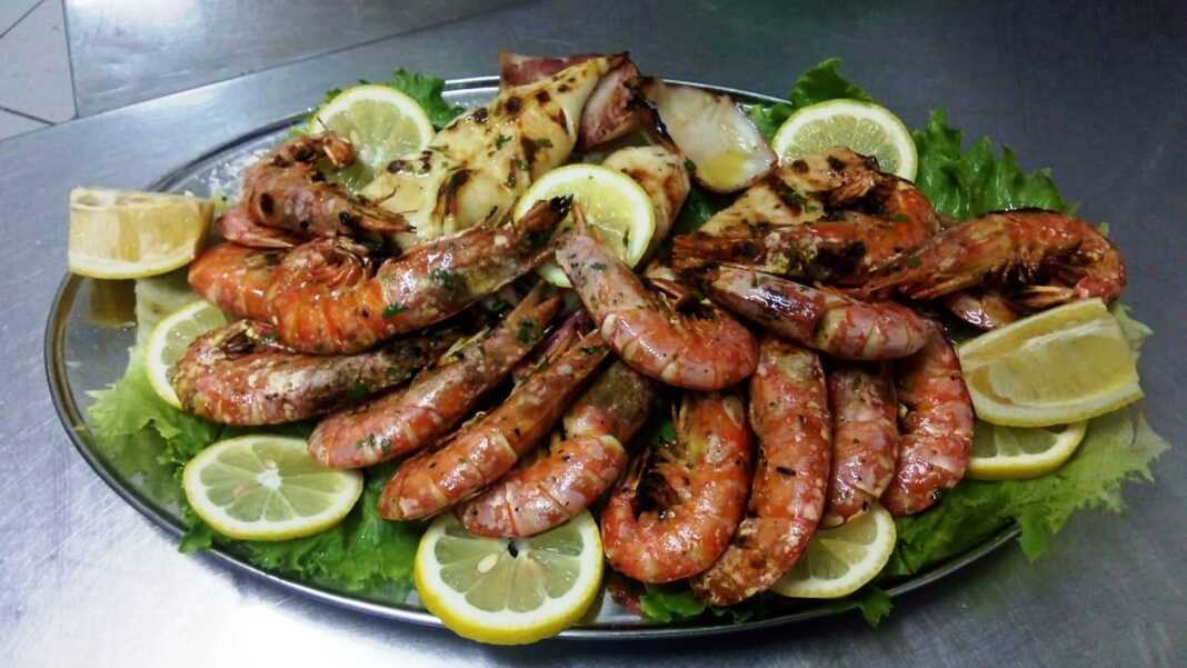 Πιάτο με ψητές γαρίδες και καλαμάρια, γαρνιρισμένα με μαϊντανό και φέτες λεμονιού, με ένα μπολ σάλτσα μουστάρδας δίπλα.