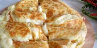 Μια σπιτική Κασερόπιτα με πατάτα σε ξύλο κοπής, κομμένη σε κομμάτια, έτοιμη για σερβίρισμα.