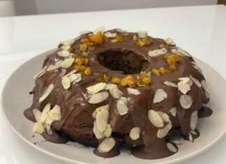 Ένα λαχταριστό κομμάτι υγρό κέικ σοκολάτας με πορτοκάλι καλυμμένο με πλούσιο γλάσο και στολισμένο με φιλέ αμυγδάλου και ξύσμα