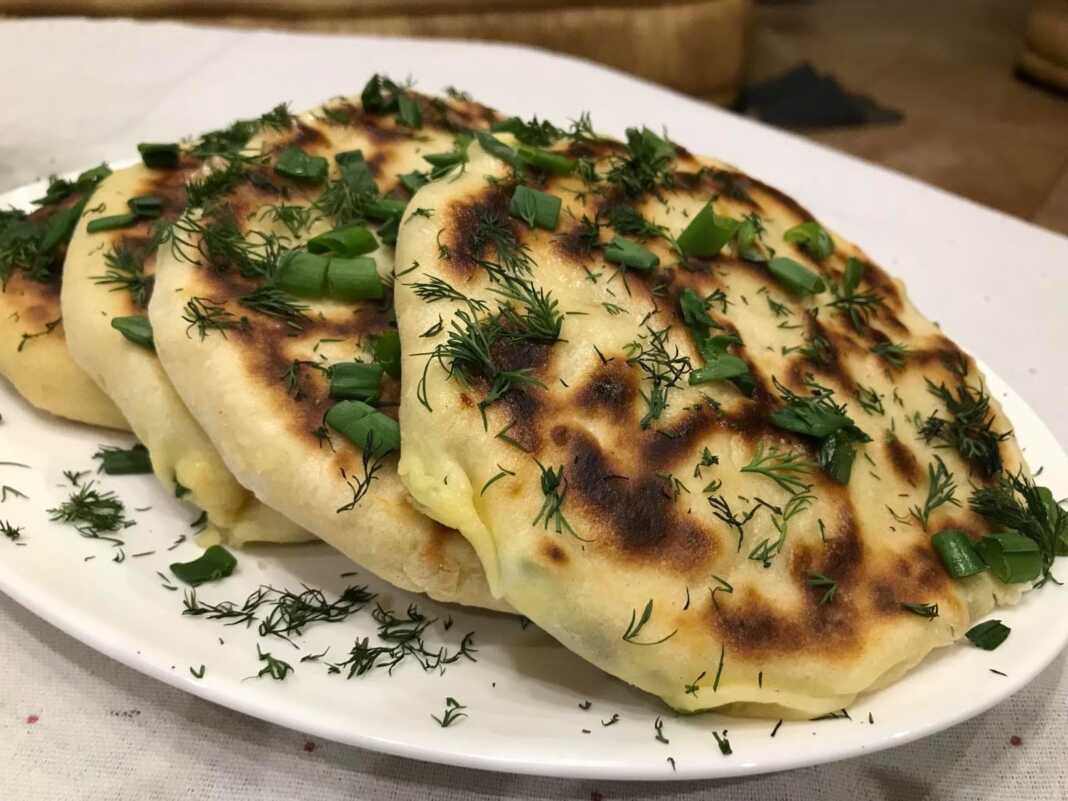 Μια στοίβα από χρυσαφένιες, τηγανισμένες πίτες με γέμιση τυριού, τοποθετημένες σε ξύλινη επιφάνεια.