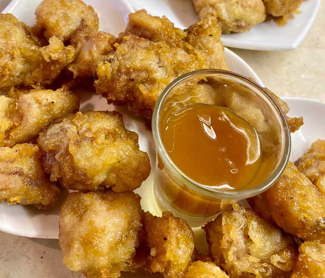 Ένα πιάτο με χρυσαφένιες, τραγανές μπουκιές κοτόπουλου περιχυμένες με γυαλιστερή καραμελωμένη σάλτσα, πασπαλισμένες με σουσάμι.