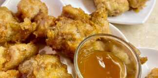 Ένα πιάτο με χρυσαφένιες, τραγανές μπουκιές κοτόπουλου περιχυμένες με γυαλιστερή καραμελωμένη σάλτσα, πασπαλισμένες με σουσάμι.