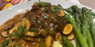 Ζουμερά Μπιφτέκια σε σάλτσα μανιταριών, σερβιρισμένα με πουρέ πατάτας και πράσινα σπαράγγια, πασπαλισμένα με μαϊντανό.