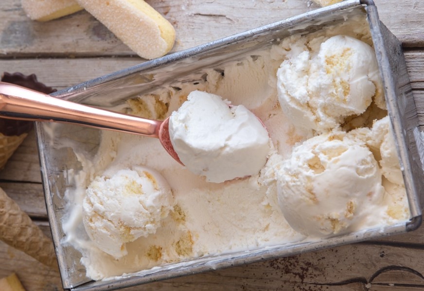 pagotoTirmisou Ένα μπολ με παγωτό τιραμισού πασπαλισμένο με κακάο, δίπλα σε μερικά κομμάτια σαβαγιάρ.