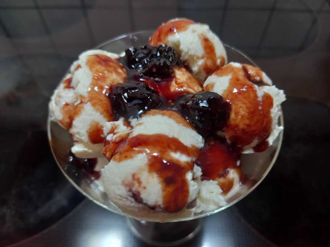 Ένα μπολ γεμάτο με κρεμώδες λευκό παγωτό γιαούρτι, με στροβιλισμούς από κόκκινο σιρόπι βύσσινο στην επιφάνεια.