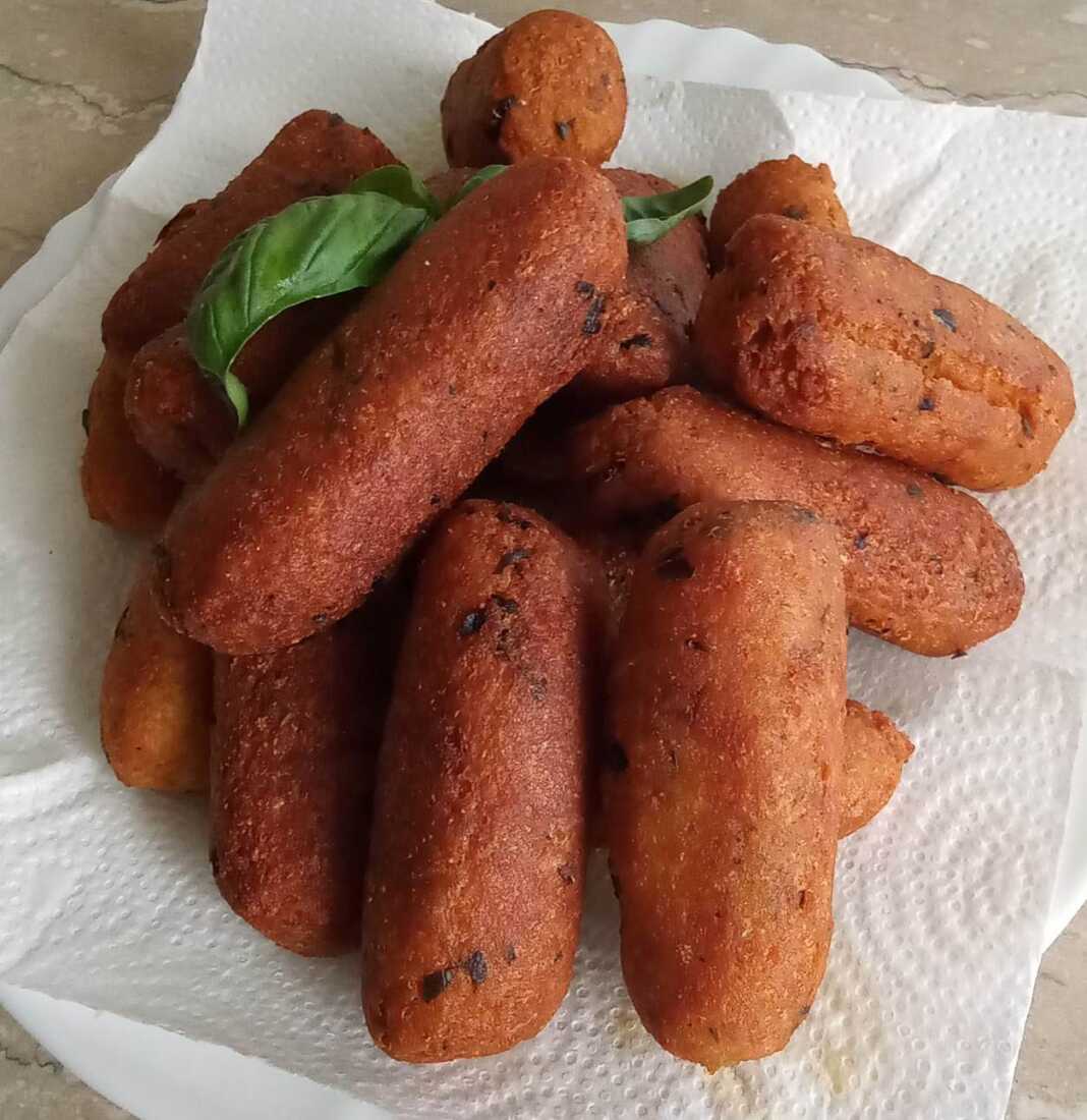 Μια στοίβα από χρυσαφένιους, τηγανητούς μελιτζανοκεφτέδες σε ένα πιάτο, γαρνιρισμένους με φρέσκα μυρωδικά.