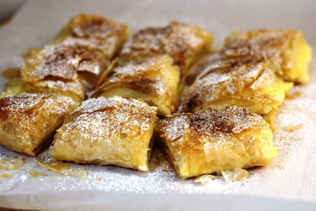 Μπουγάτσα με κρέμα, πασπαλισμένη με άχνη ζάχαρη και κανέλα, κομμένη σε κομμάτια.