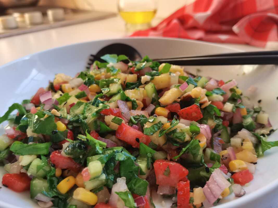 Έγχρωμη σαλάτα του καλοκαιριού σε ένα μπολ, με ρόκα, καλαμπόκι, ανανά, φράουλες, αγγούρι και θρυμματισμένα αμύγδαλα, γαρνιρισμένη με μαύρο σουσάμι.