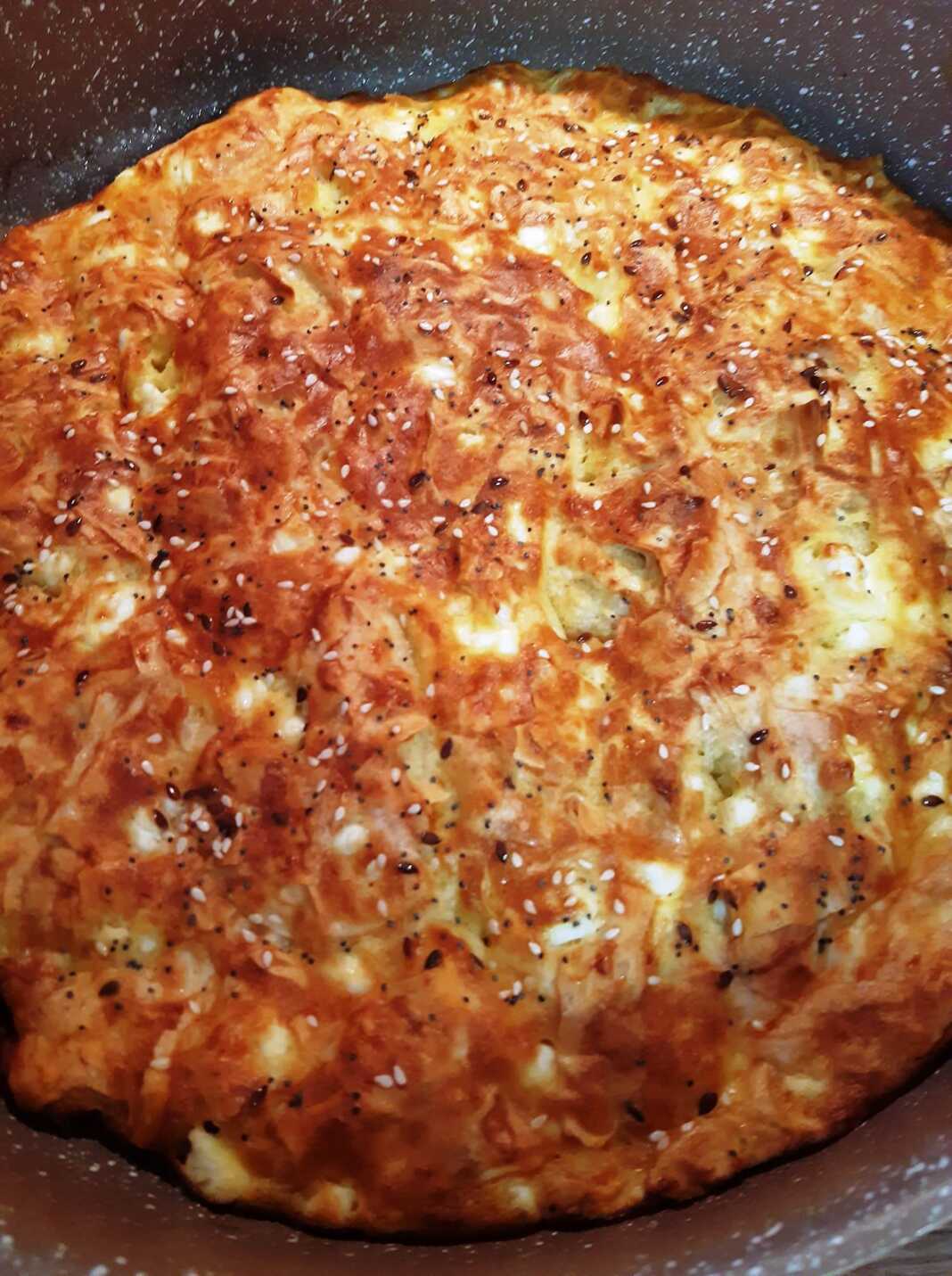 Χρυσαφένια και αφράτη τεμπέλικη τυρόπιτα μέσα σε ταψί με διάσπαρτους σπόρους στην επιφάνεια