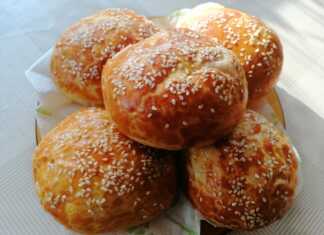 Δίσκος με ροδοκοκκινισμένα στρογγυλά τυροπιτάκια πασπαλισμένα με σουσάμι τοποθετημένα πάνω σε αντικολλητικό χαρτί