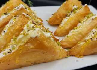 Τραγανά χρυσαφένια τρίγωνα από φύλλο κρούστας, γεμισμένα με λευκή κρέμα τυριού, γαρνιρισμένα με ρευστό μέλι και πράσινο φιστίκι Αιγίνης.