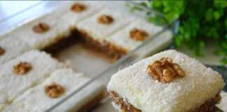 Ένα κομμάτι σιροπιαστού γλυκού με μια στρώση σαν κέικ από κάτω, μια παχιά στρώση λευκής κρέμας στη μέση και πασπαλισμένο με άφθονη τριμμένη καρύδα στην κορυφή.