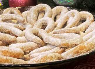 Μικρά κουλουράκια σε σχήμα πετάλου καλυμμένα με άχνη ζάχαρη τοποθετημένα σε μια πιατέλα δίπλα σε ολόκληρα καρύδια