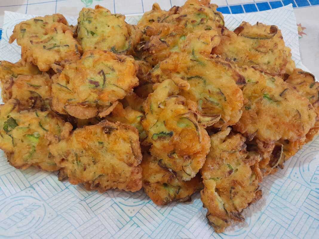 tiganitesKolokithoantoi Χρυσαφένιες, τραγανές τηγανίτες με κολοκυθοανθούς σε πιάτο, γαρνιρισμένες με φρέσκο βασιλικό, σε ρουστίκ φόντο.