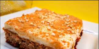 Ένα κομμάτι καρυδόπιτας με μια στρώση λευκής κρέμας βανίλιας από πάνω, πασπαλισμένο με κανέλα και χοντροκομμένα καρύδια.