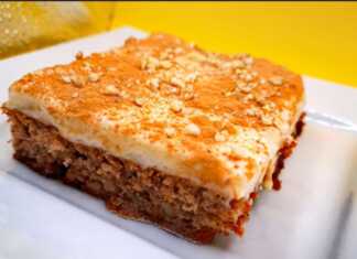 Ένα κομμάτι καρυδόπιτας με μια στρώση λευκής κρέμας βανίλιας από πάνω, πασπαλισμένο με κανέλα και χοντροκομμένα καρύδια.