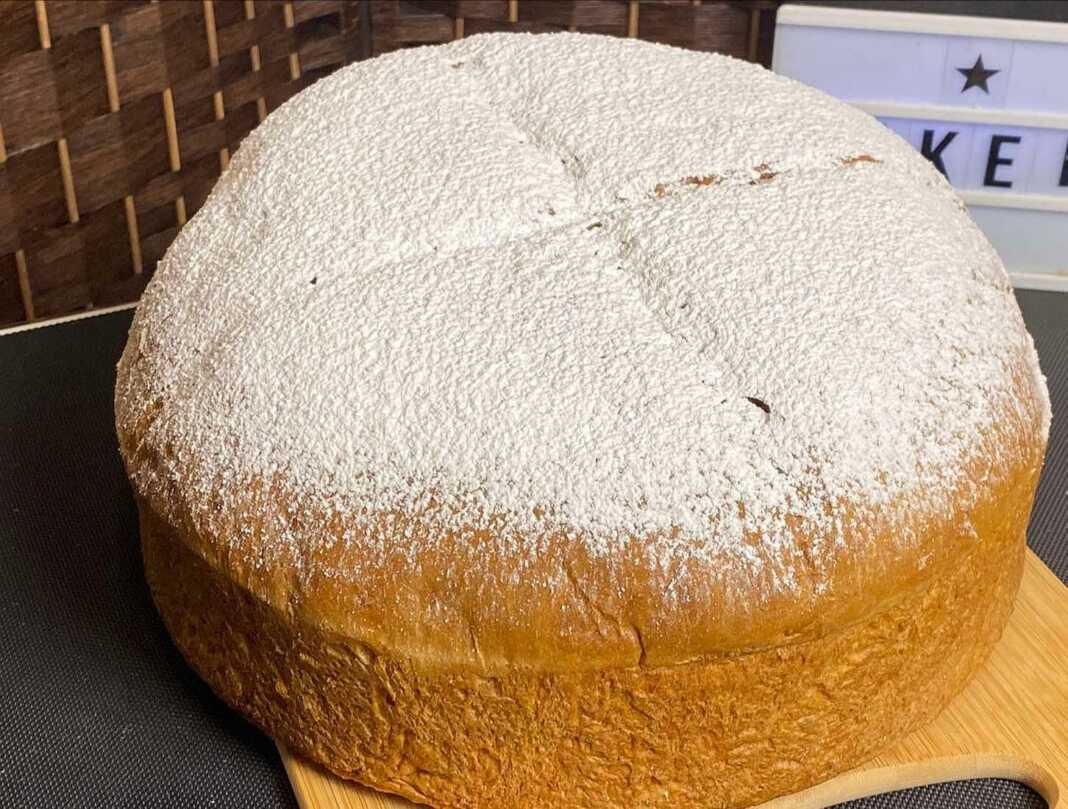 Ολόκληρη Μπουγάτσα της Παναγίας, χρυσαφένια και αφράτη, πασπαλισμένη με ζάχαρη άχνη, σε ξύλινη επιφάνεια