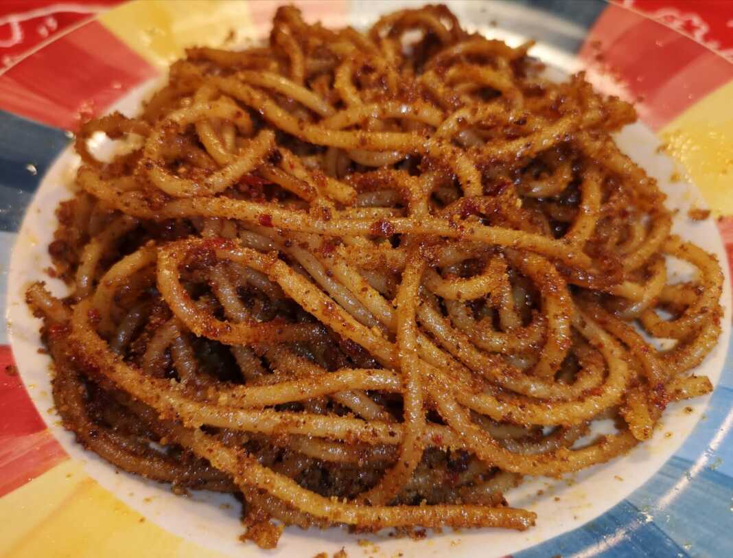 Σκορδομακαρονάδα με αντσούγιες, πασπαλισμένη με τραγανή φρυγανιά, σερβιρισμένη σε πιάτο.