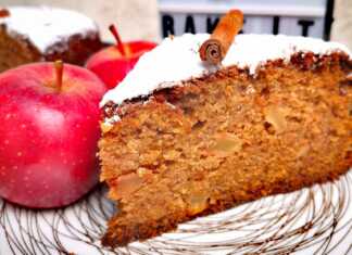 Υψηλή, αφράτη φέτα μηλόπιτας με ορατά κομμάτια μήλου και καρυδιών, πασπαλισμένη με ζάχαρη άχνη.