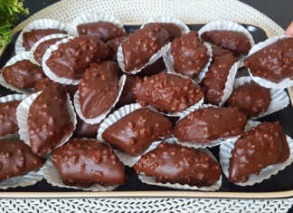 Ένα ταψί με λαδόκολλα γεμάτο με σκουρόχρωμα, σοκολατένια μπισκότα, μερικά από τα οποία είναι ήδη βουτηγμένα σε λιωμένη σοκολάτα και πασπαλισμένα με αμύγδαλα.