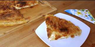 Μια χρυσαφένια, φρεσκοψημένη τυρόπιτα με εμφανή στρώματα φύλλου, κομμένη σε τετράγωνα κομμάτια, που αναδεικνύει την τραγανή της υφή.