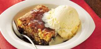 Ένα κομμάτι καφέ κέικ σε ένα άσπρο πιάτο, με σκούρα σάλτσα καραμέλας να το σιροπιάζει