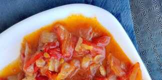 Ένα πιάτο με κομμάτια κοτόπουλου ανακατεμένα με χρωματιστές πιπεριές σε κόκκινη σάλτσα ντομάτας.