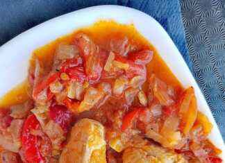 Ένα πιάτο με κομμάτια κοτόπουλου ανακατεμένα με χρωματιστές πιπεριές σε κόκκινη σάλτσα ντομάτας.