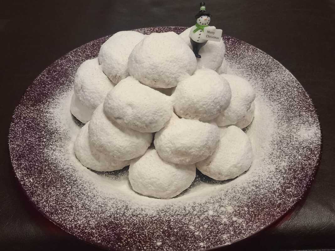 Πιατέλα με χιονισμένους Κουραμπιέδες πασπαλισμένους με άχνη, με εμφανή τα χοντροκομμένα αμύγδαλα.