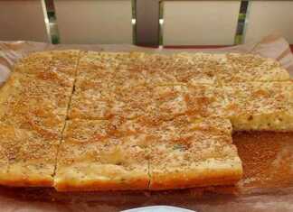 Αφράτη, ψηλή τυρόπιτα-κέικ, κομμένη σε τετράγωνα κομμάτια, με θρυμματισμένη φέτα και πασπαλισμένη με σουσάμι.