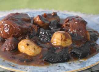 Αγριογούρουνο κοκκινιστό με μελωμένη σάλτσα κρασιού, ολόκληρα δαμάσκηνα και μανιτάρια, σερβιρισμένο σε πιατέλα με φόντο χριστουγεννιάτικη διακόσμηση.