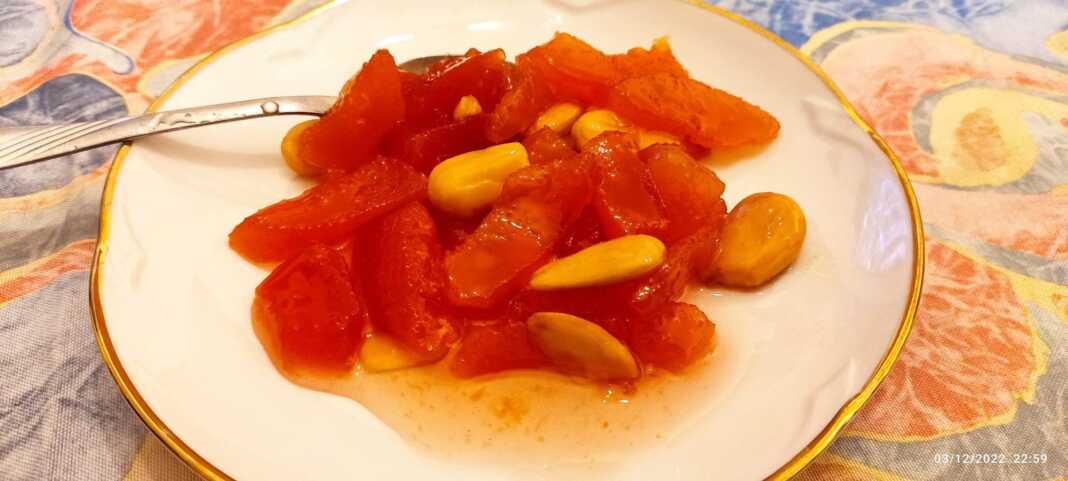 Γλυκό του κουταλιού κυδώνι σε πιατιάκι , με κομμάτια αμύγδαλου και κλωνάρι αρμπαρόριζα.