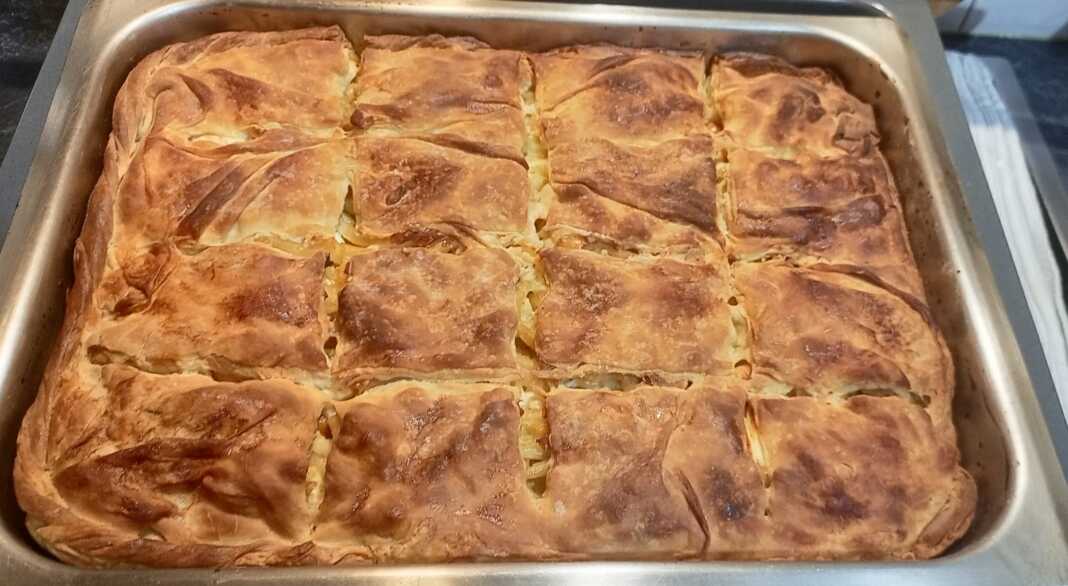 Μια χρυσαφένια, φρεσκοψημένη μακαρονόπιτα με σπιτικό φύλλο, κομμένη σε τετράγωνα κομμάτια, έτοιμη για σερβίρισμα.