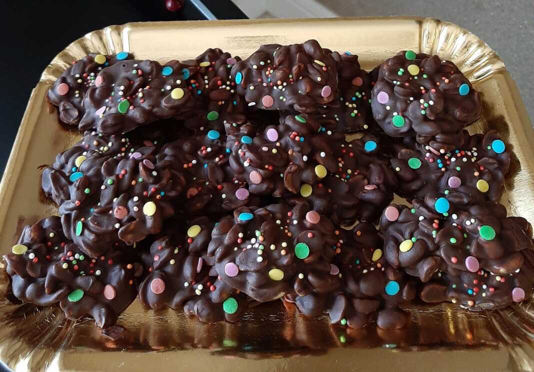 Μικροί σωροί από αλατισμένα φιστίκια καλυμμένα με σκούρα και λευκή σοκολάτα, τοποθετημένα σε λαδόκολλα, με χρωματιστά κουφετάκια για διακόσμηση.