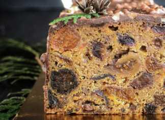 Πλούσιο χριστουγεννιάτικο κέικ γεμάτο με σταφίδες, ξηρούς καρπούς και ζαχαρωμένα φρούτα, διακοσμημένο με λευκό γλάσο και γιορτινά μούρα