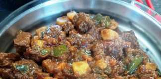 Ένα πιάτο με πλούσιο, κόκκινο μοσχαρίσιο γκούλας με κομμάτια κρέατος και πατάτες, γαρνιρισμένο με φρέσκα μυρωδικά.