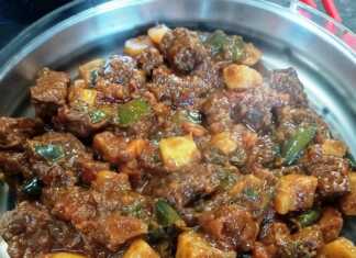 Ένα πιάτο με πλούσιο, κόκκινο μοσχαρίσιο γκούλας με κομμάτια κρέατος και πατάτες, γαρνιρισμένο με φρέσκα μυρωδικά.