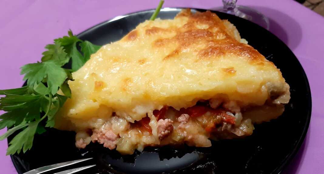 Μια χρυσαφένια Πίτα του Βοσκού σε κεραμικό ταψί, με τριμμένο τυρί στην επιφάνεια και φρέσκα μυρωδικά στο πλάι.