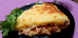 Μια χρυσαφένια Πίτα του Βοσκού σε κεραμικό ταψί, με τριμμένο τυρί στην επιφάνεια και φρέσκα μυρωδικά στο πλάι.