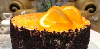 Ένα Κεικ πολύστρωτο με βάση σοκολάτας, ενδιάμεσες στρώσεις λευκής κρέμας τυριού και πορτοκαλί γλάσου, και ψίχουλα κέικ στα πλαϊνά.