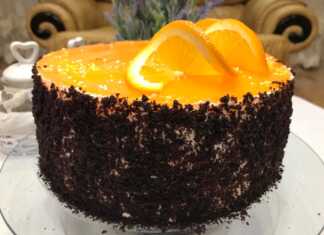 Ένα Κεικ πολύστρωτο με βάση σοκολάτας, ενδιάμεσες στρώσεις λευκής κρέμας τυριού και πορτοκαλί γλάσου, και ψίχουλα κέικ στα πλαϊνά.