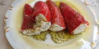 Γυάλινο βάζο γεμάτο με κόκκινες πιπεριές Φλωρίνης γεμιστές με λευκό τυρί, βυθισμένες σε λάδι, με ένα φύλλο δάφνης και σκελίδα σκόρδου ορατά.