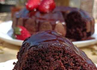 Ένα κομμάτι από αφράτο, σκούρο καφέ κέικ σοκολάτας, περιχυμένο με γυαλιστερό σοκολατένιο γλάσο, σερβιρισμένο σε λευκό πιάτο.