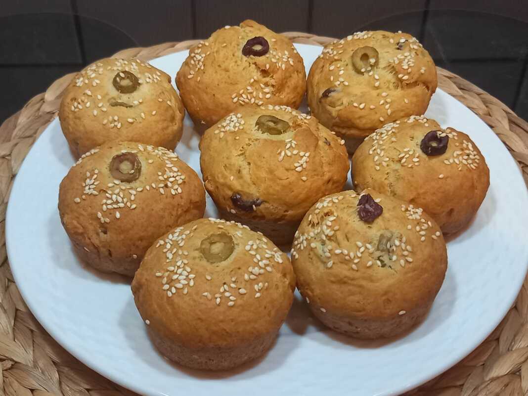 Μικρά ροδοκοκκινισμένα νηστίσιμα ελιοπιτάκια πασπαλισμένα με σουσάμι, αραδιασμένα πάνω σε αντικολλητικό χαρτί ψησίματος