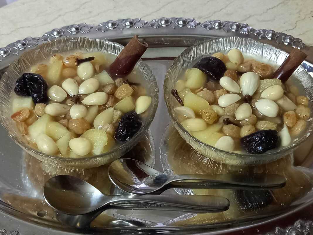 kousafi Μπολ με ζεστό Κουσάφι, γεμάτο φρούτα και αρωματισμένο με κανέλα, στολισμένο με αμύγδαλα.