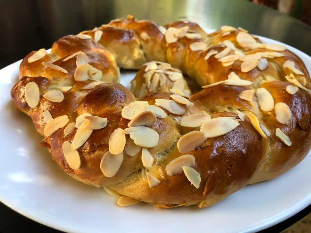 Χρυσαφένιο πλεξούδα τσουρέκι πασπαλισμένο με νιφάδες αμυγδάλου πάνω σε ξύλινη επιφάνεια