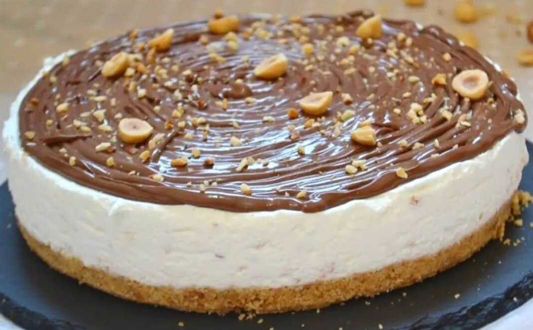 Μια τούρτα γιαουρτιού με στρώσεις κρέμας και διακόσμηση από πραλίνα φουντουκιού και ολόκληρα φουντούκια.