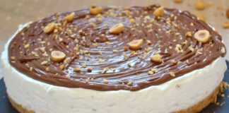 Μια τούρτα γιαουρτιού με στρώσεις κρέμας και διακόσμηση από πραλίνα φουντουκιού και ολόκληρα φουντούκια.